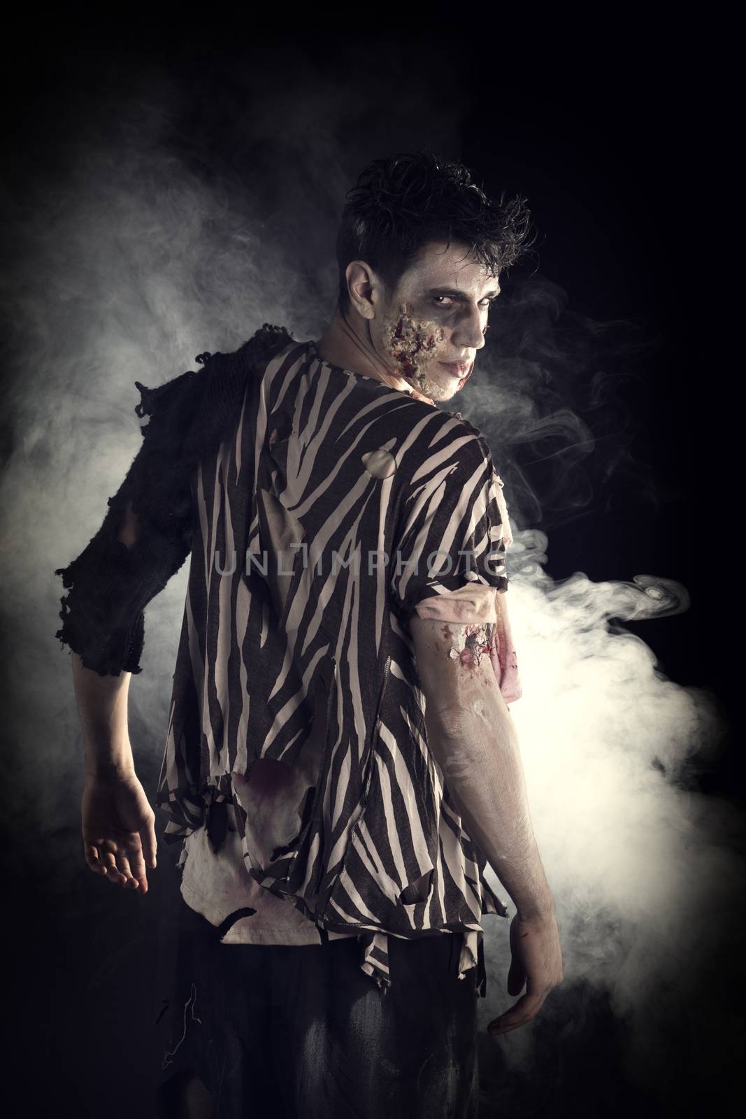 Male zombie standing on black background, turning around looking at camera. Halloween theme