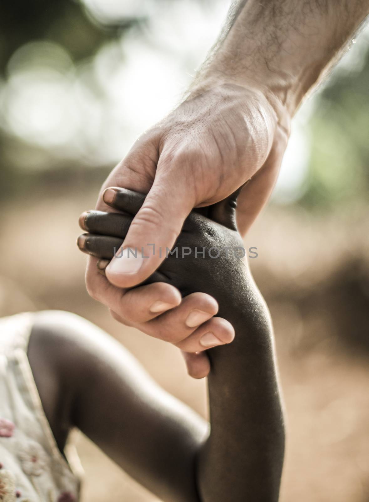 An african child holding a white males hand. The image represents the care and love in diversity and a cross cultural relationship