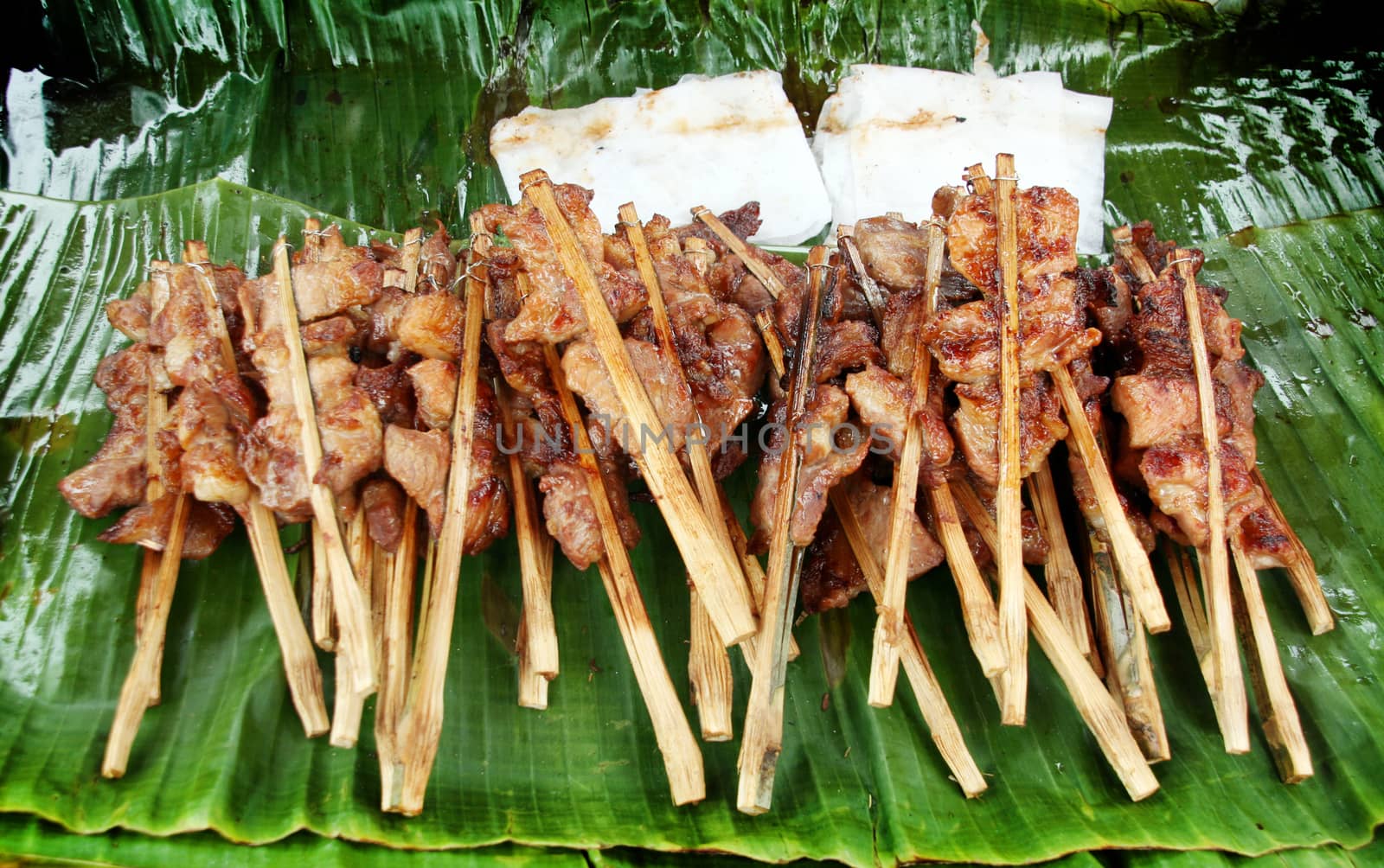 close up roasted pork with wood stick and sticky rice on banana leaf on street shop