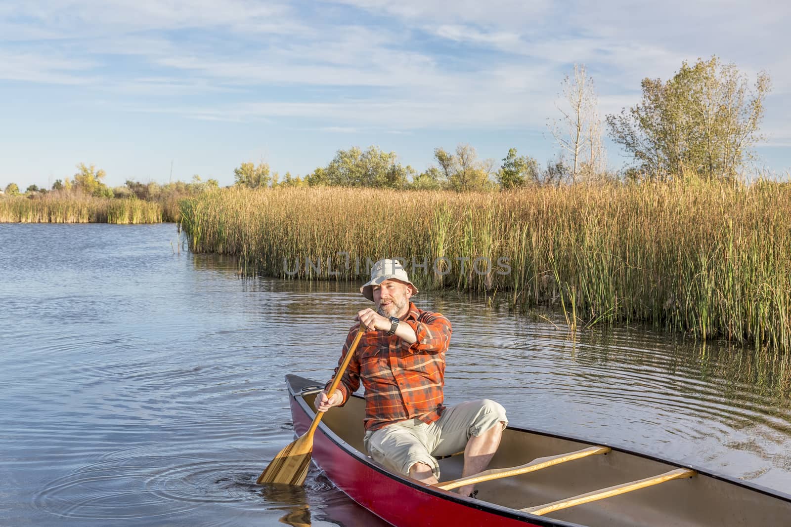 senior paddler enjoying paddling a red canoe on a calm lake, Riverbend Ponds Natural Area, Fort Collins, Colorado