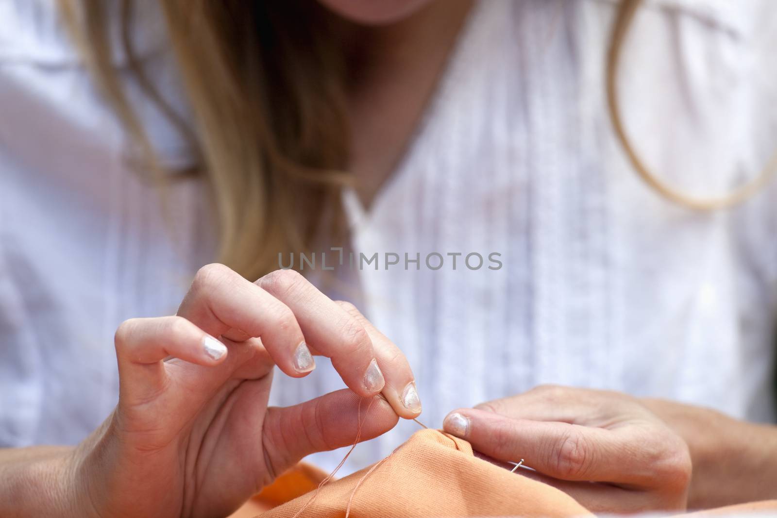 closeup of womans hands sewing orange cloth outdoors