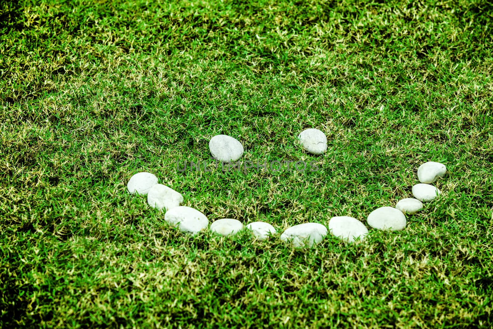 arranging white stone on the green grass in smile concept for eco background