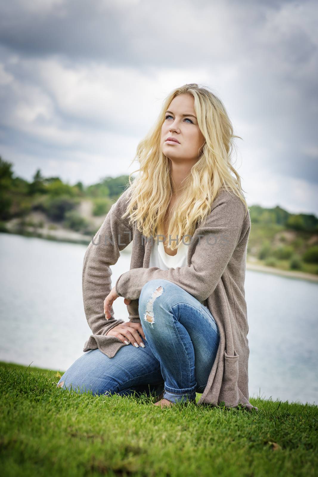 Blond woman kneeling on a grean meadow at the edge of a lake in summer