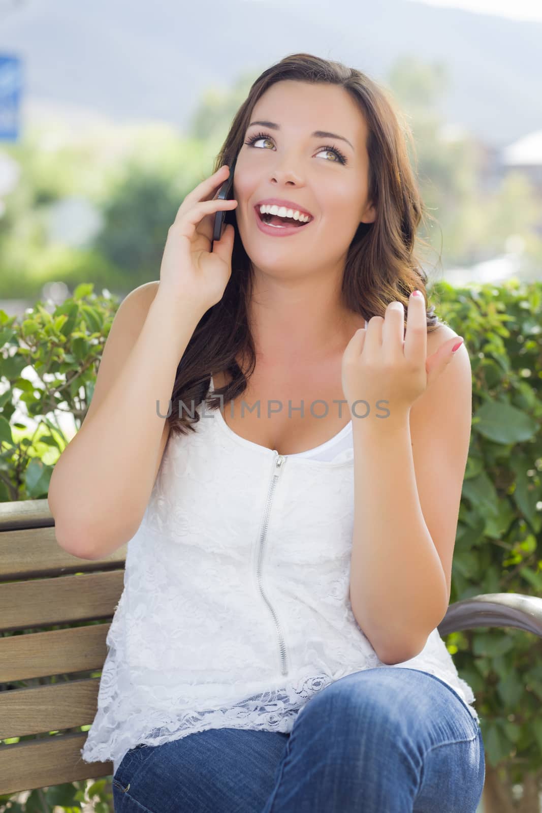 Attractive Young Adult Female Talking on Cell Phone Outdoors on Bench.