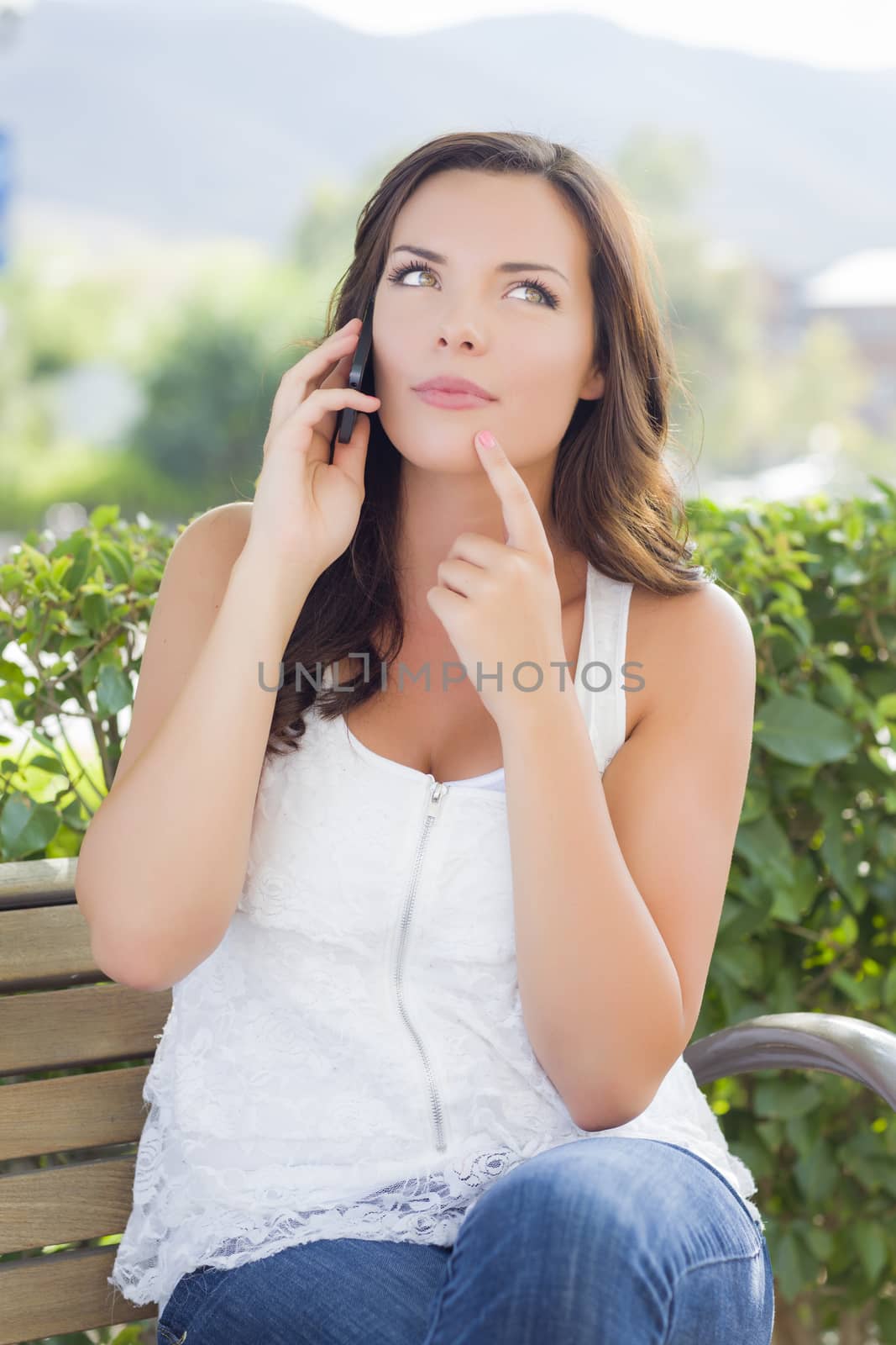 Attractive Contemplative Young Adult Female Talking on Cell Phone Outdoors on Bench.