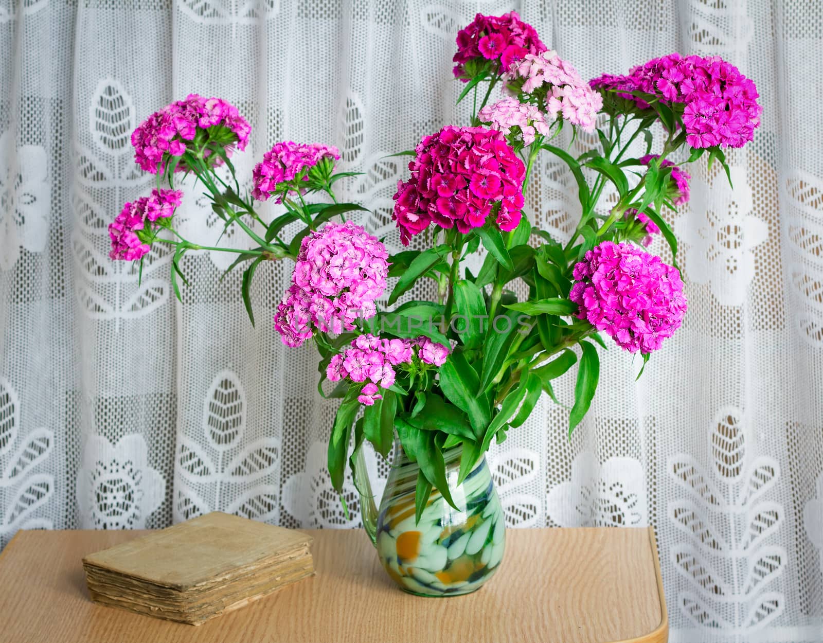  Still life: a beautiful bright pink and red flowers carnations in a glass vase on the table next to the old book.