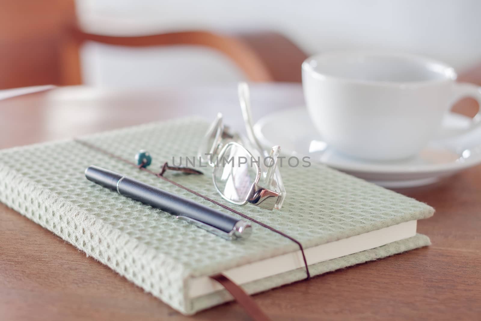 Notebook with pen, eyeglasses and white coffee cup on wooden table, stock photo