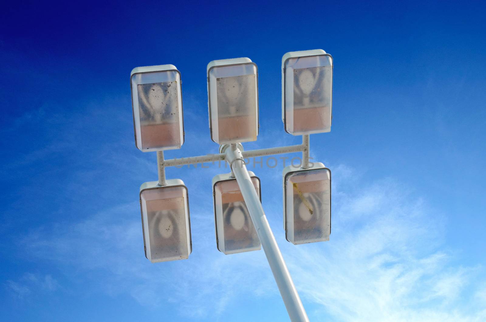 Large street lamp with six lamps in front of blue sky.