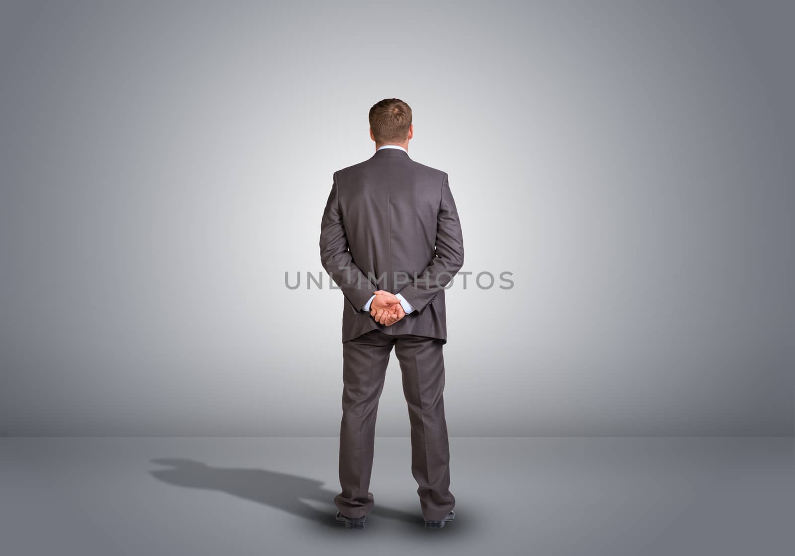 Businessman standing in an empty gray room. Rear view by cherezoff