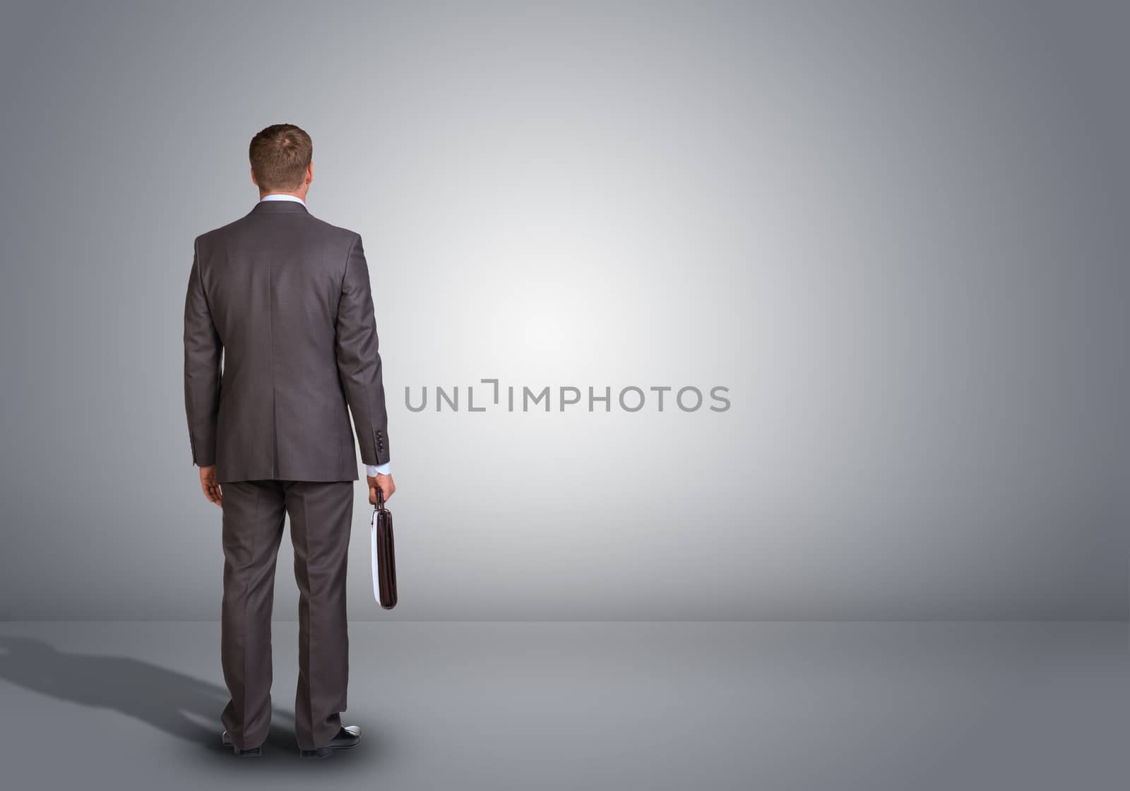 Businessman standing in an empty gray room. Rear view by cherezoff