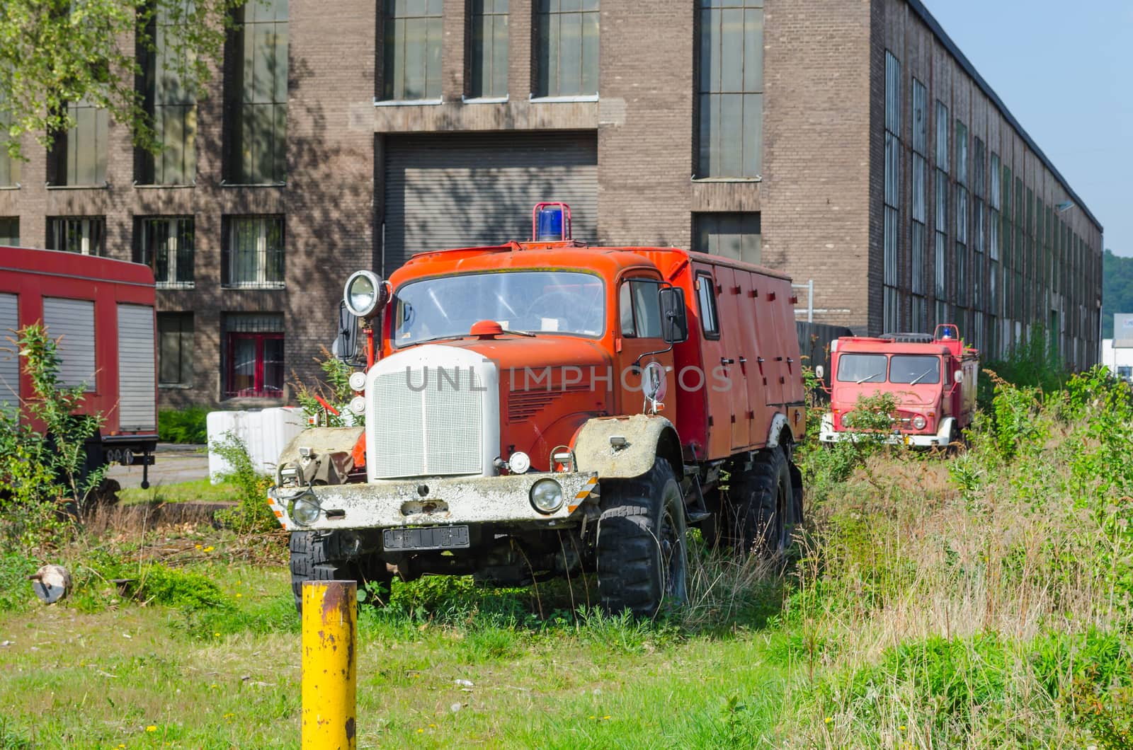 Old abandoned fire truck on a meadow in front of an old factory building.
