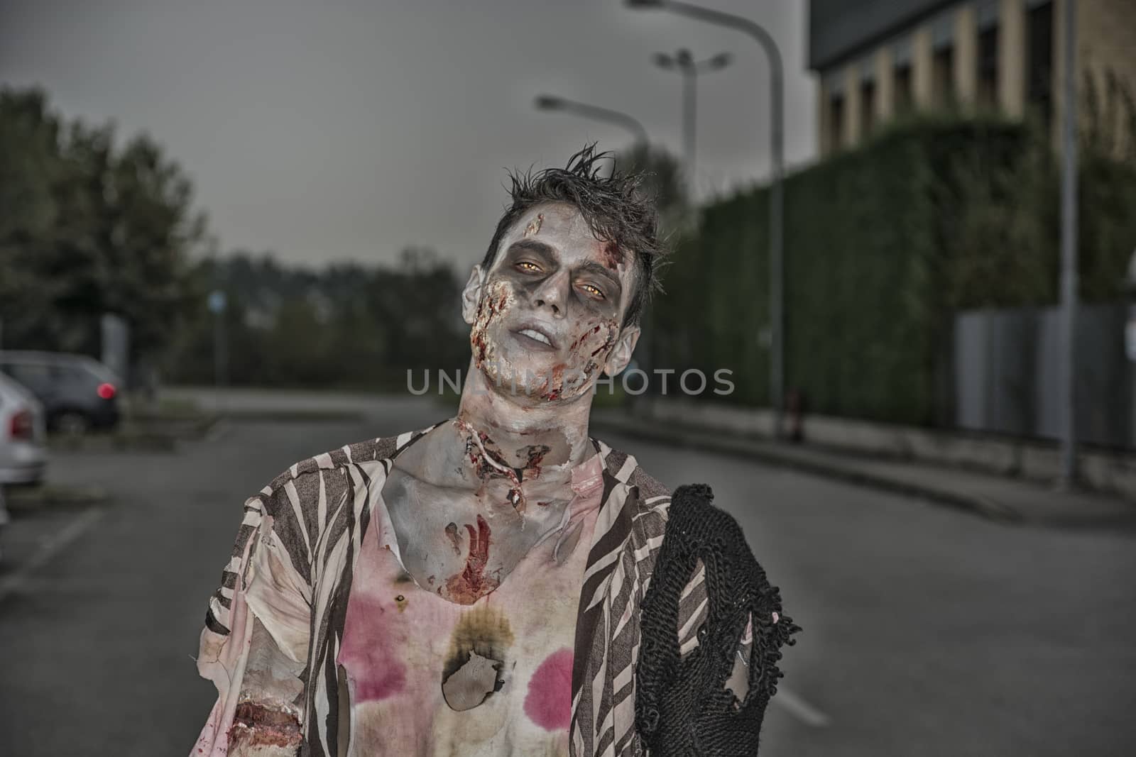 One male zombie standing in empty city street at night looking at camera. Halloween theme
