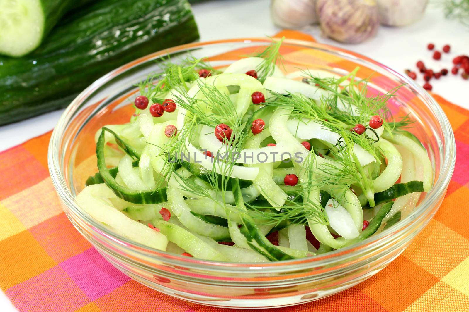 a bowl of cucumber salad with dill and red pepper berries