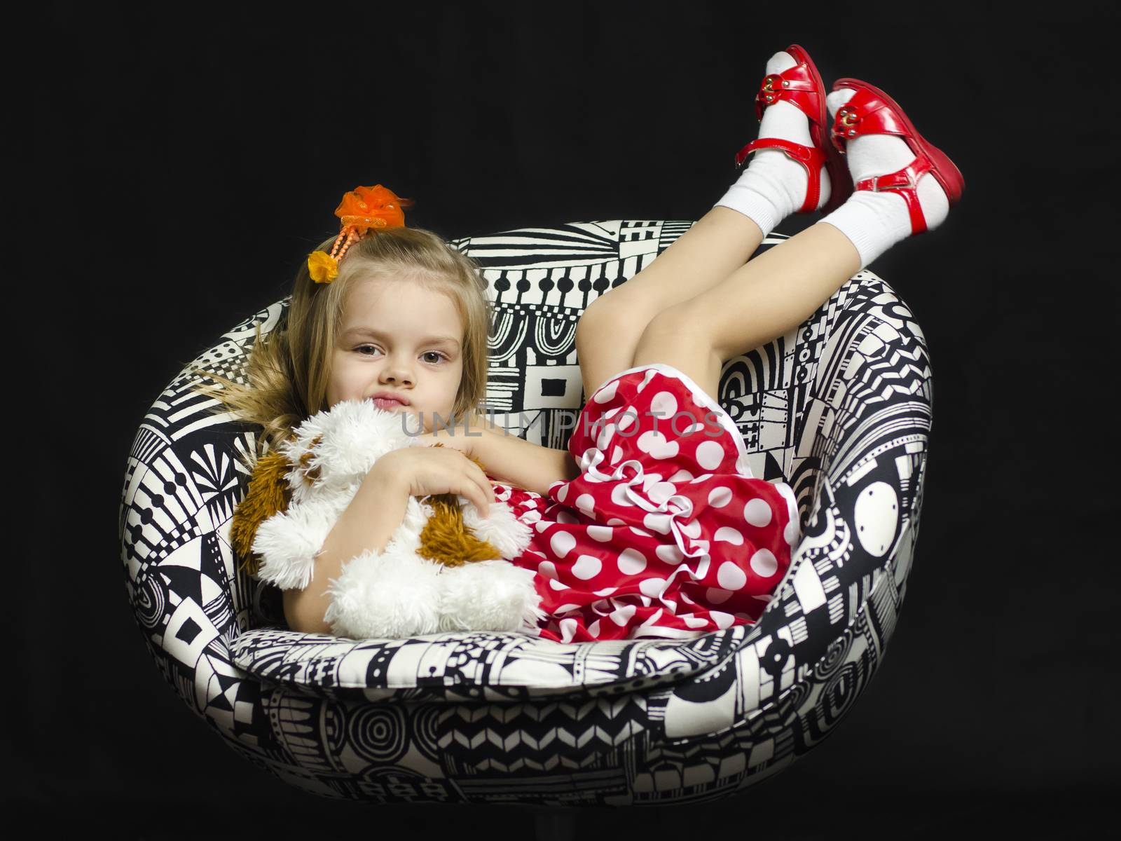 A little girl with a soft toy on a chair