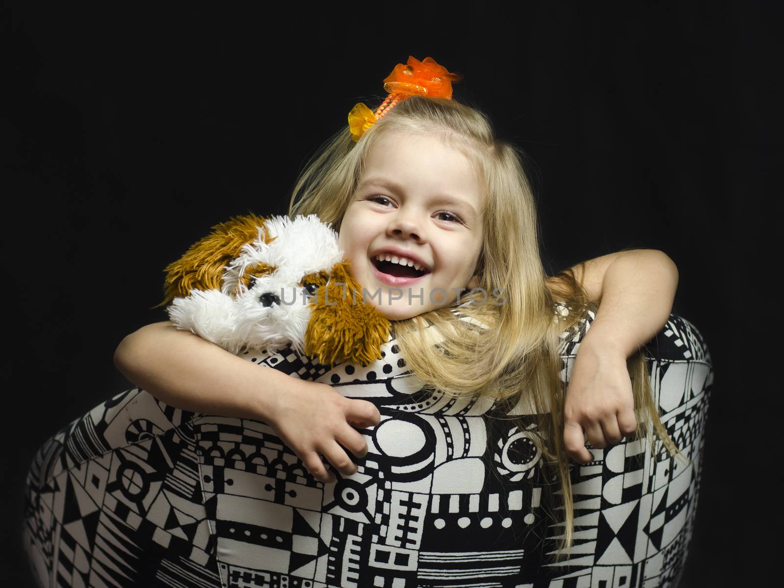 A little girl with a soft toy in the chair. The chair is deployed. The girl leaned back in her chair, hands hanging down, armpit soft toy. The black background