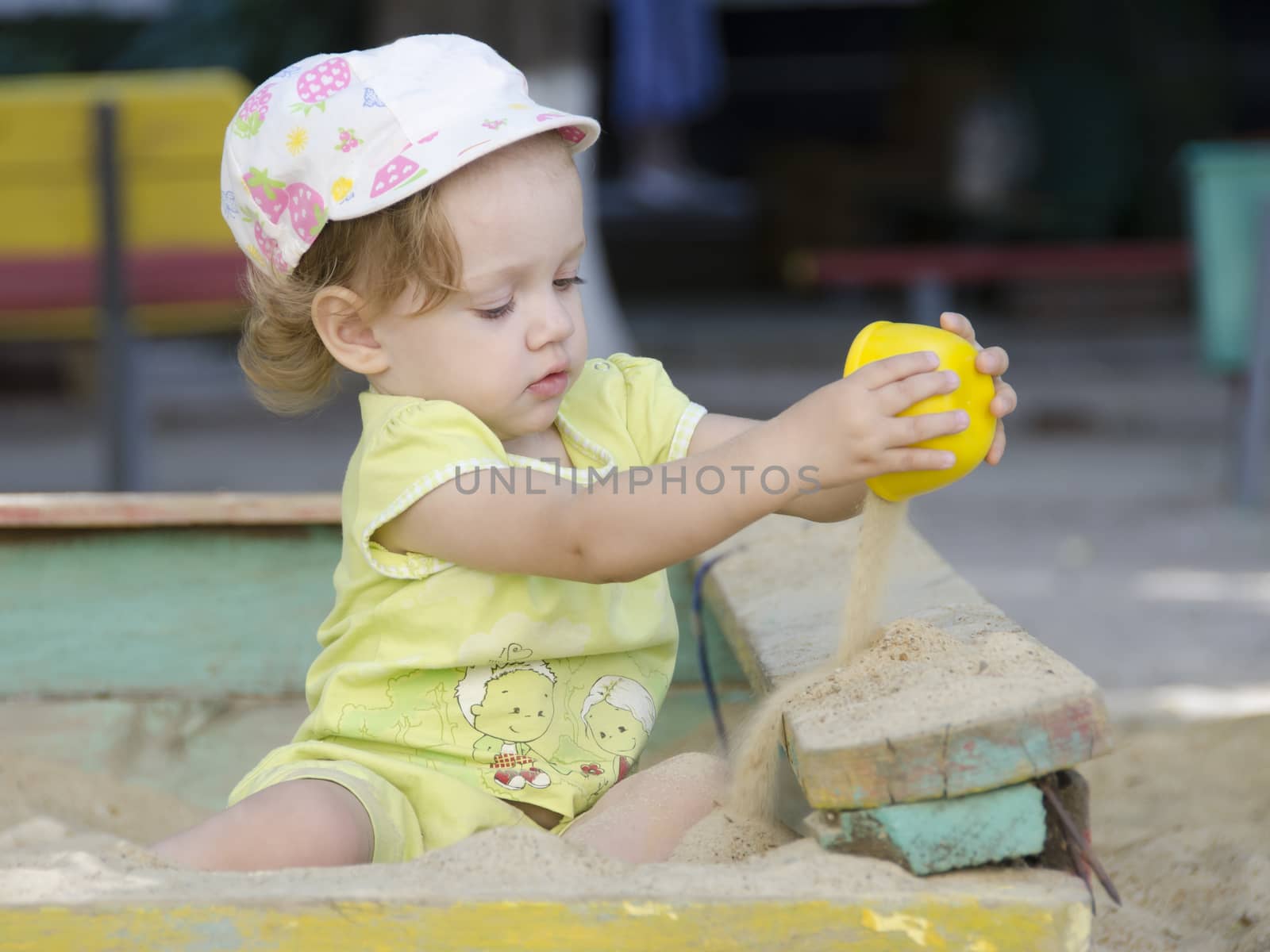 Little girl playing in the sandbox. Today the sand of the cups.