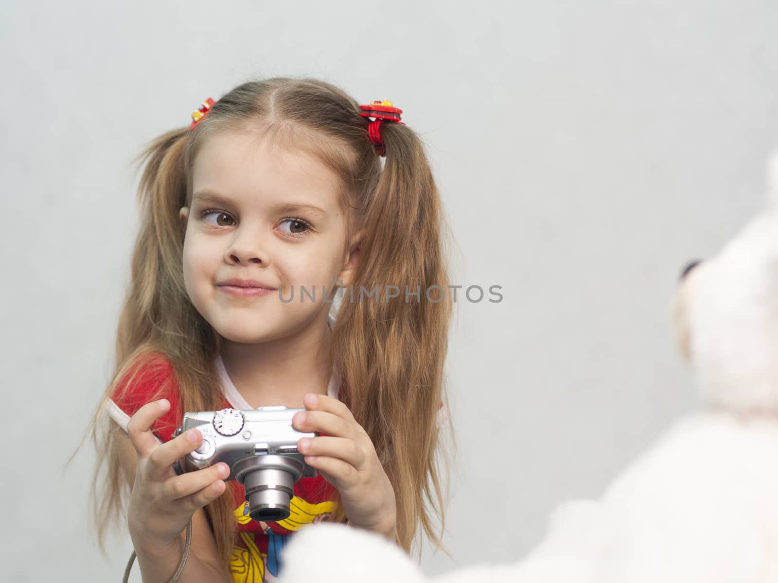 Girl playing in the photographer. Girl takes photo of Teddy digital camera and compares the result with the original.