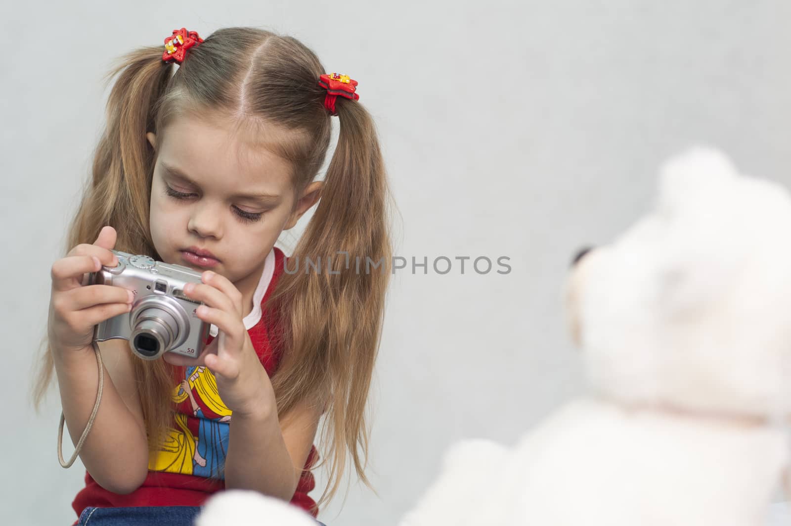 Girl playing in the photographer. Girl takes photo of Teddy digital camera and compares the result with the original