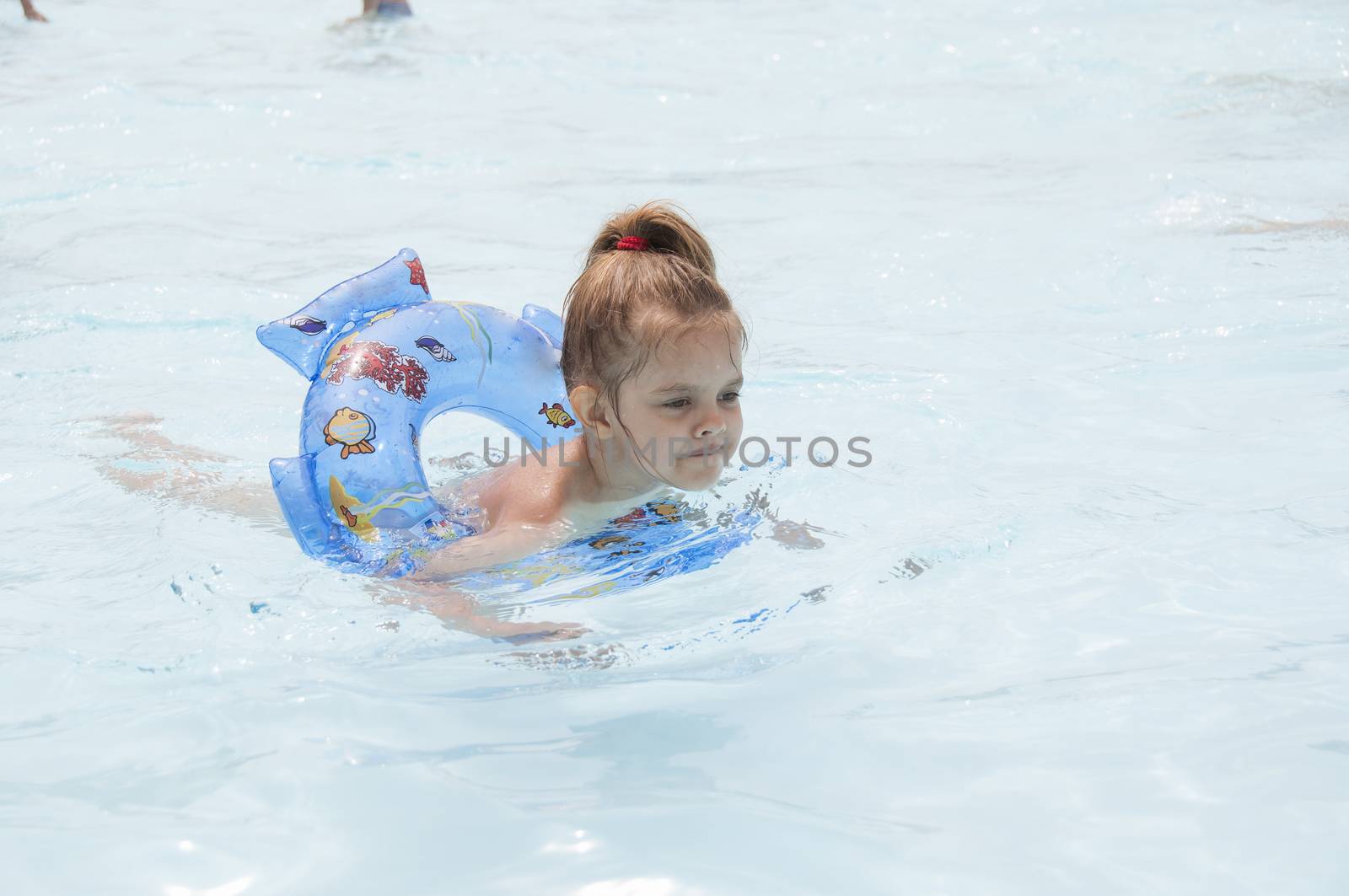 Four-year-old girl bathes in a public pool. Girl swimming on the circle. Summer day.