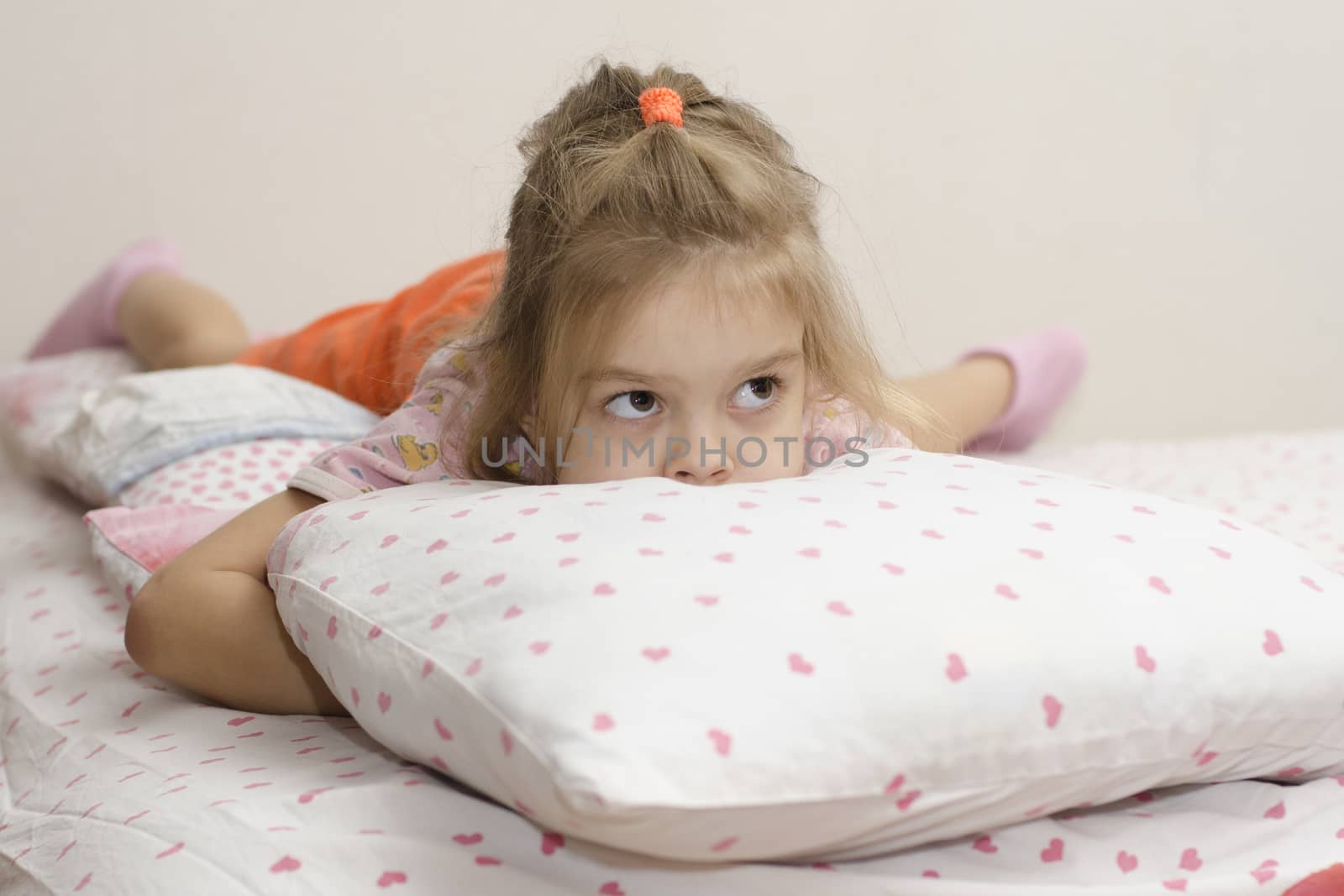 girl is lying on the bed. Buried her face in the pillow girl enthusiastically looking right. Home furnishings