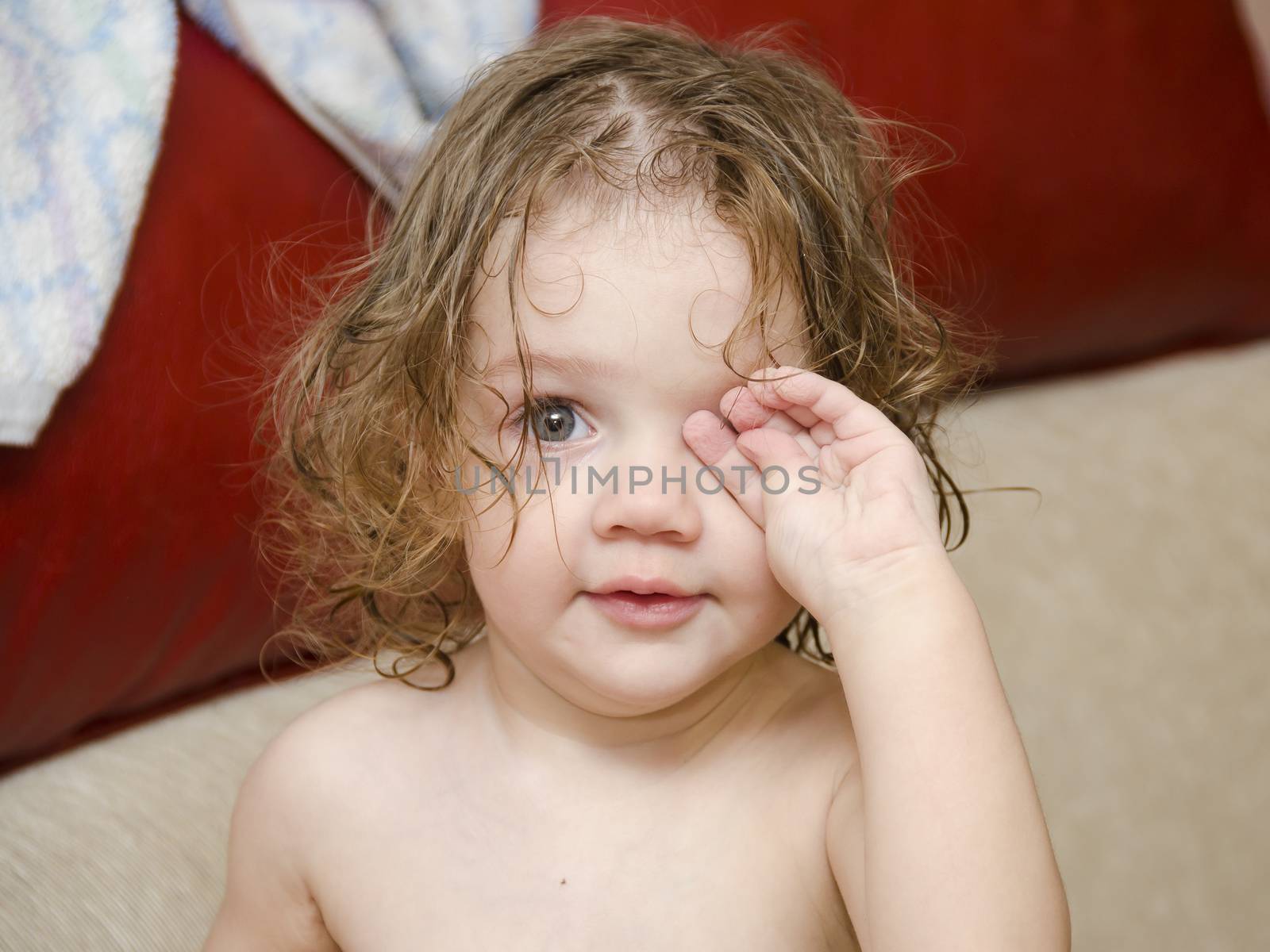 Baby wipes his eyes after swimming handle. Wet hair, drops on the face. Sitting on the couch.