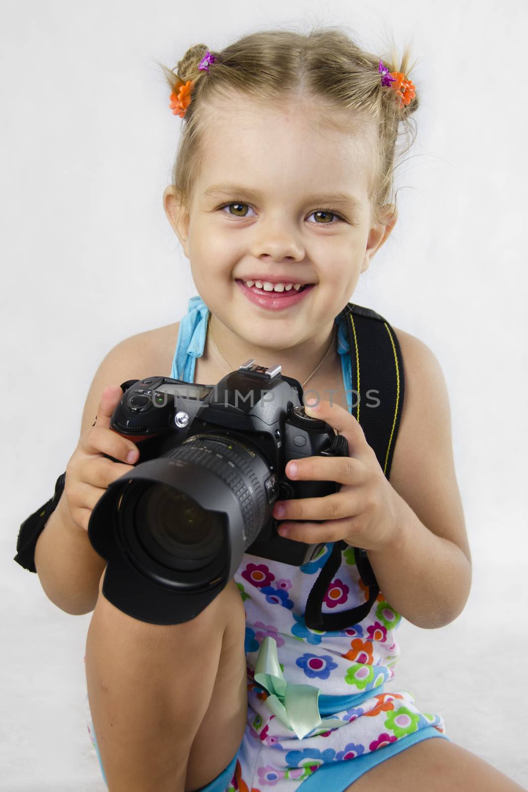 A merry girl keeps SLR camera. child rejoices, for the first time entrusted to hold the camera. The white background