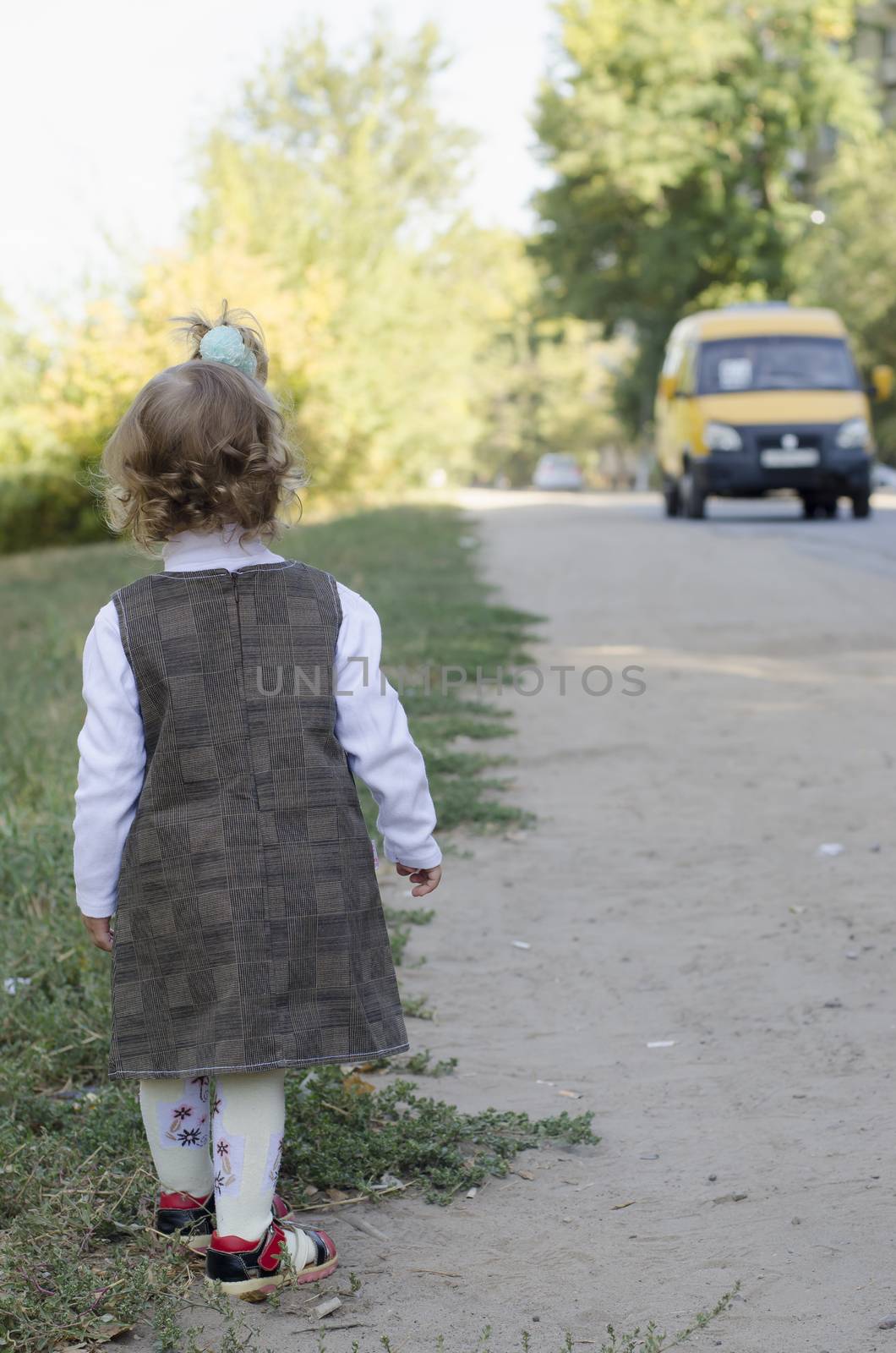 The little girl standing at the edge of the road waits for the arrival of the bus.