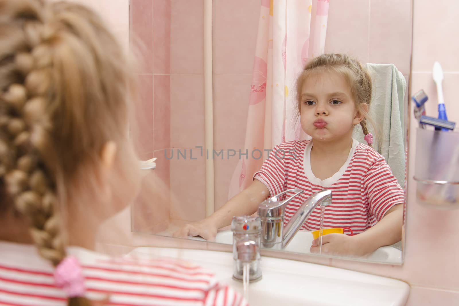 Four-year-old girl rinse your teeth after brushing. The girl looks in the mirror. Bathroom