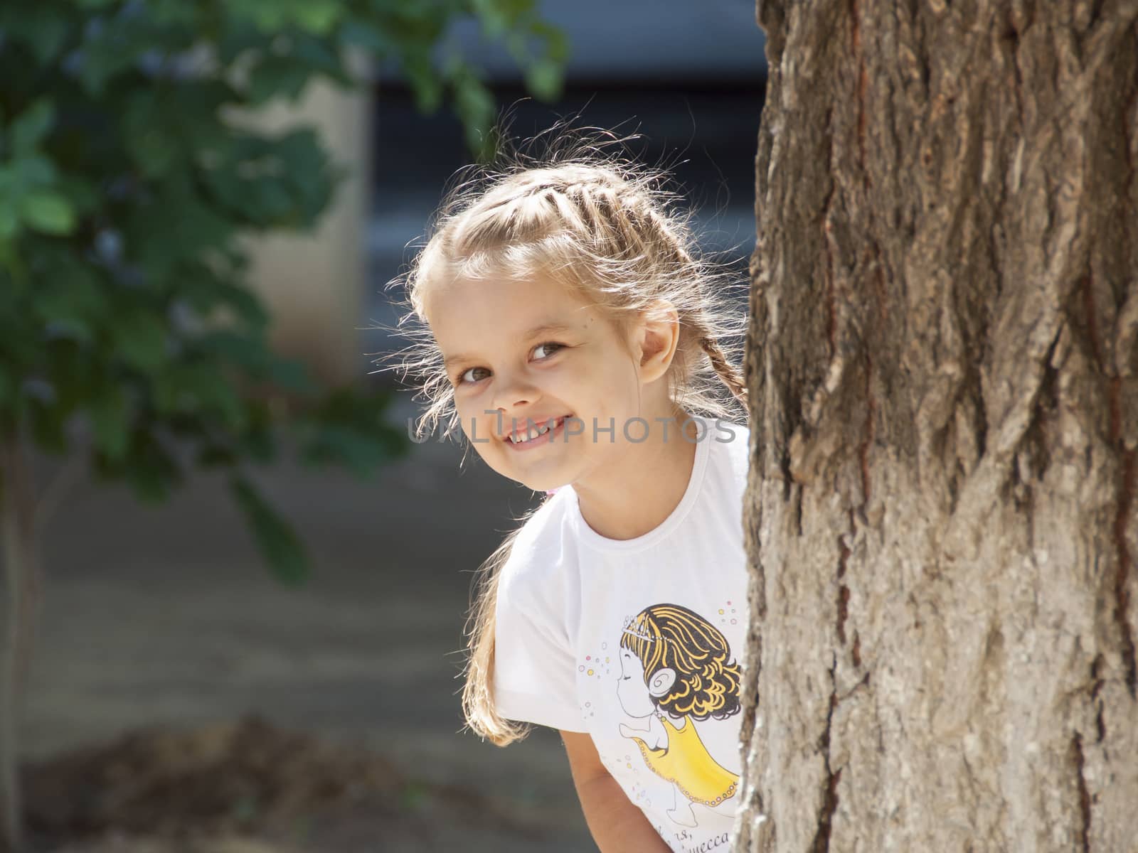 The girl with a smile peeked out from behind a tree on the left side