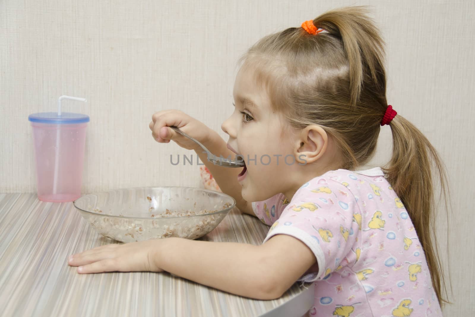 Girl eating porridge sitting at the table. The profile view. Home furnishings