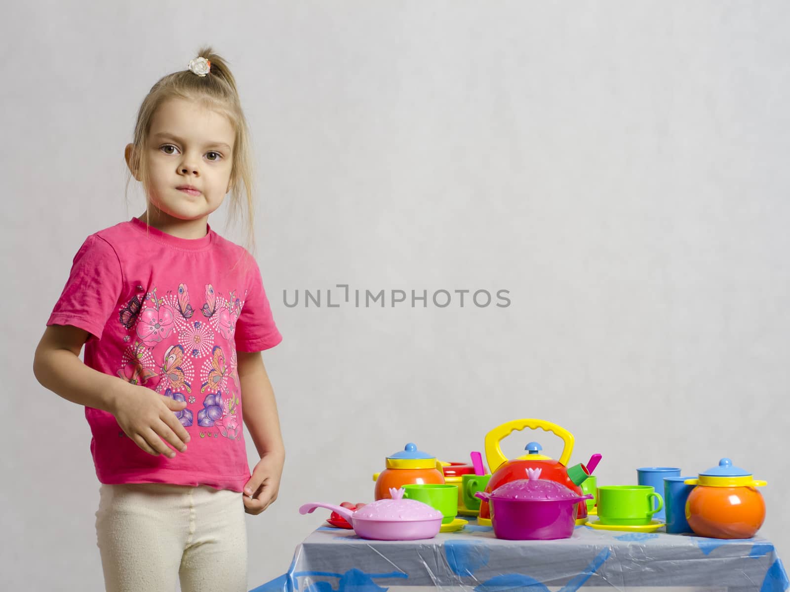 Girl plays child kitchen utensils. The girl is left of the table and looks in the frame