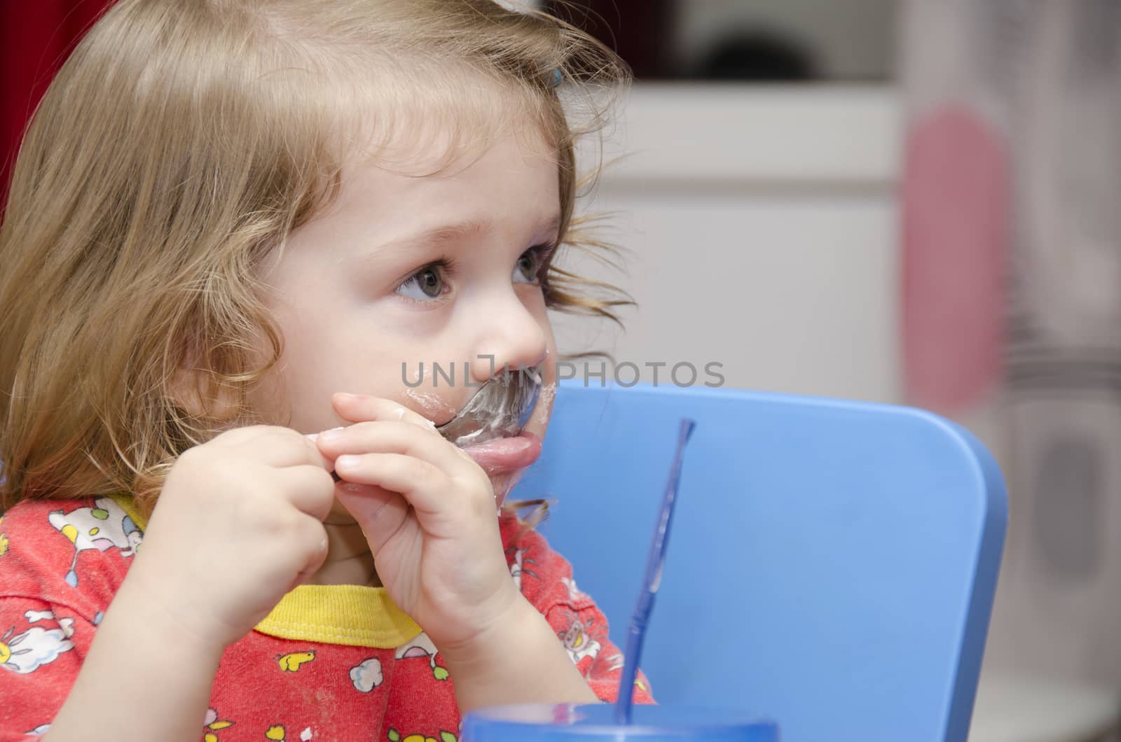 girl eats a cake sitting at the table. Passionately licks spoon and looks right. Home furnishings