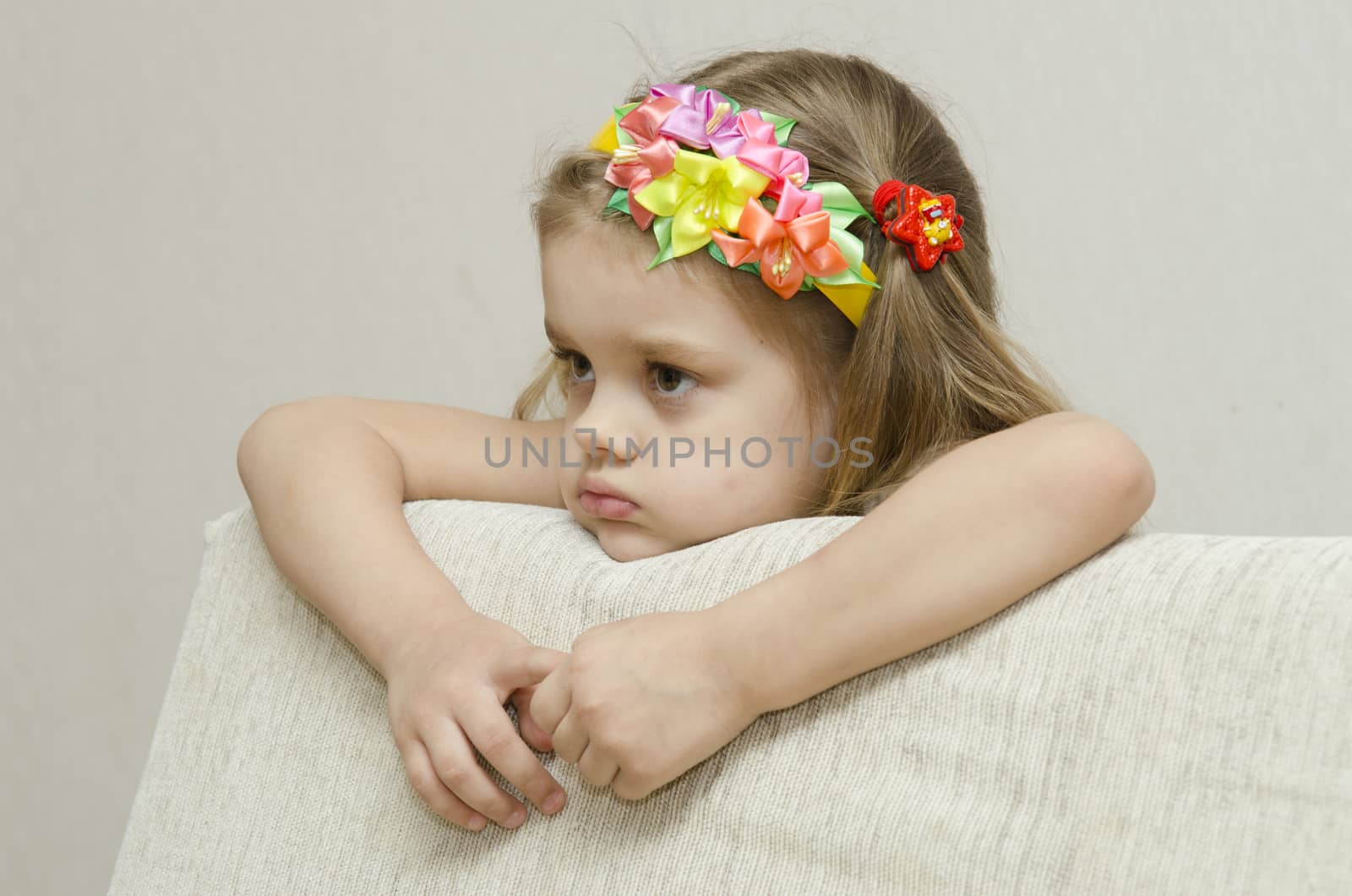 The girl thoughtfully looks to the left, his arms dangling from the back of the couch, and laid on the sofa his head. On the head of a girls band with beautiful flowers