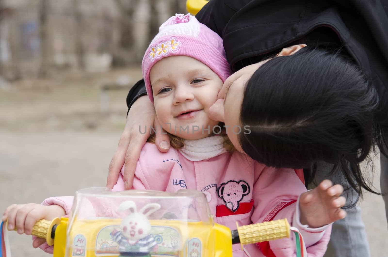A little girl sat on the bike. Mom leaned over to her and kisses her. A warm spring day.