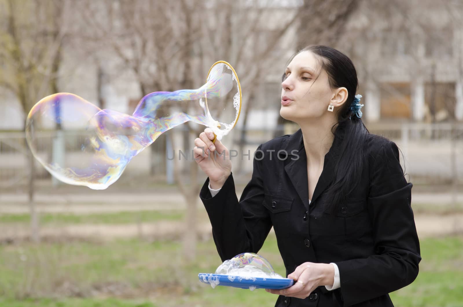 A girl inflates a big bubble. Street, early spring