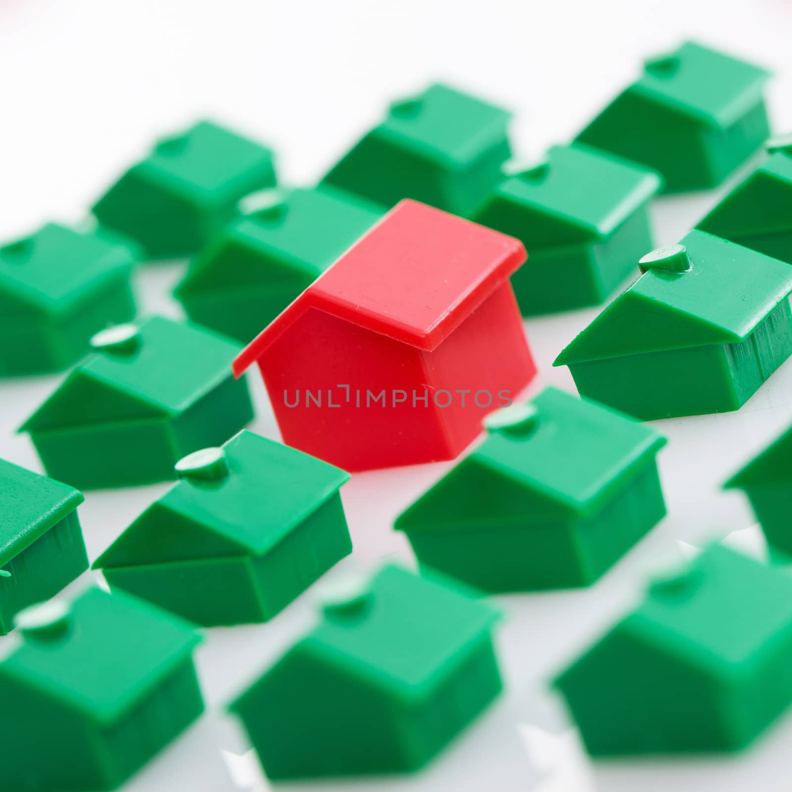 Many green toy houses and one red in the middle over a white background