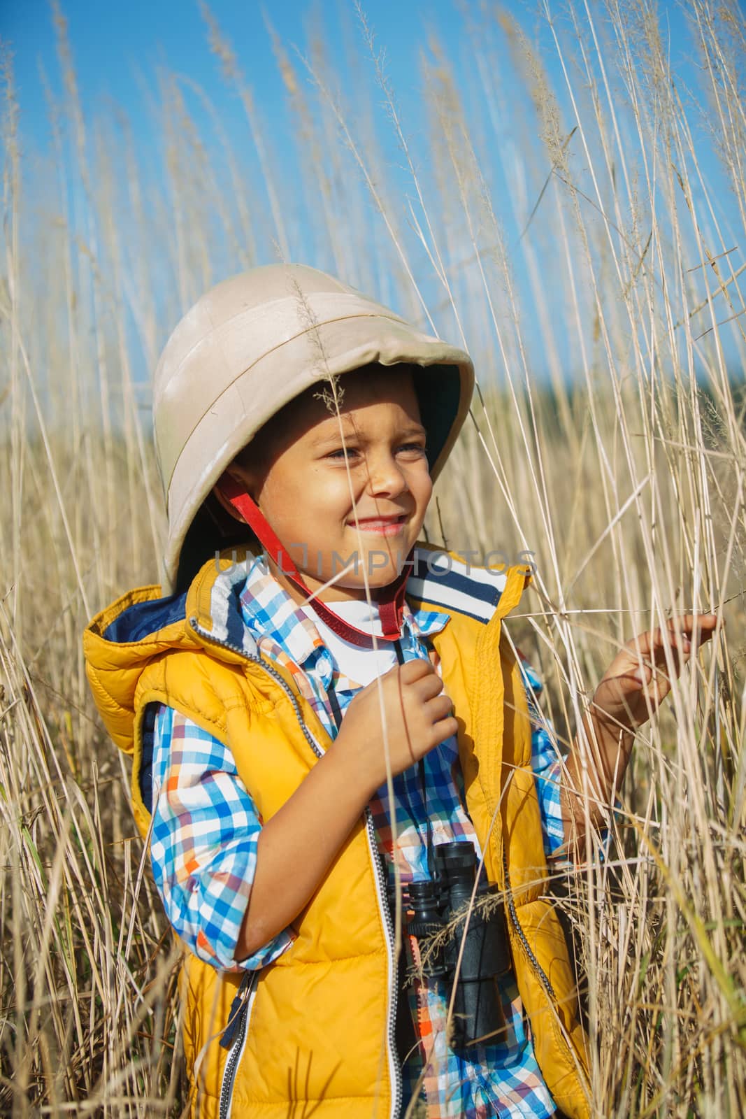 Young boy child playing pretend explorer adventure safari game outdoors with binoculars and bush hat