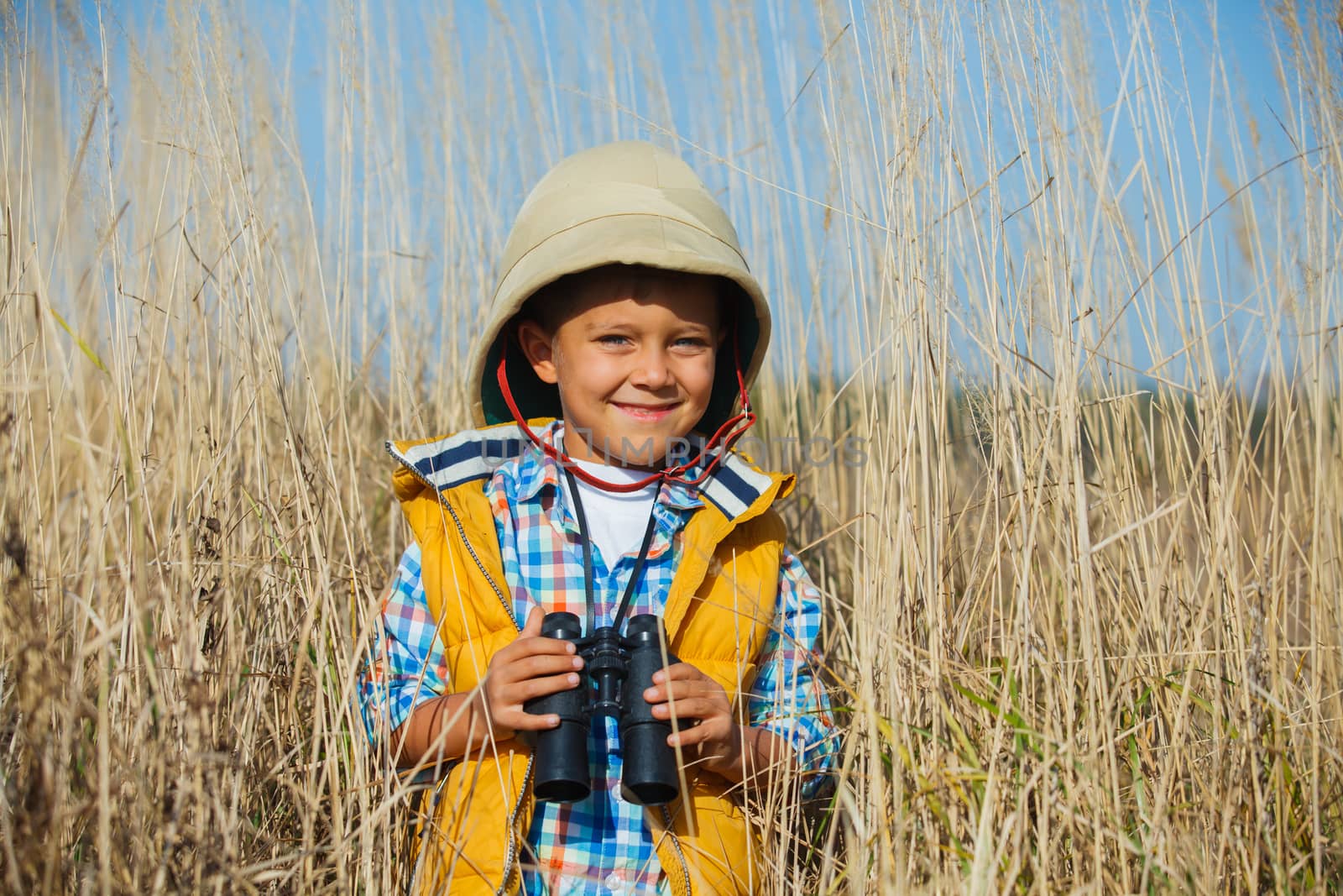 Young boy child playing pretend explorer adventure safari game outdoors with binoculars and bush hat