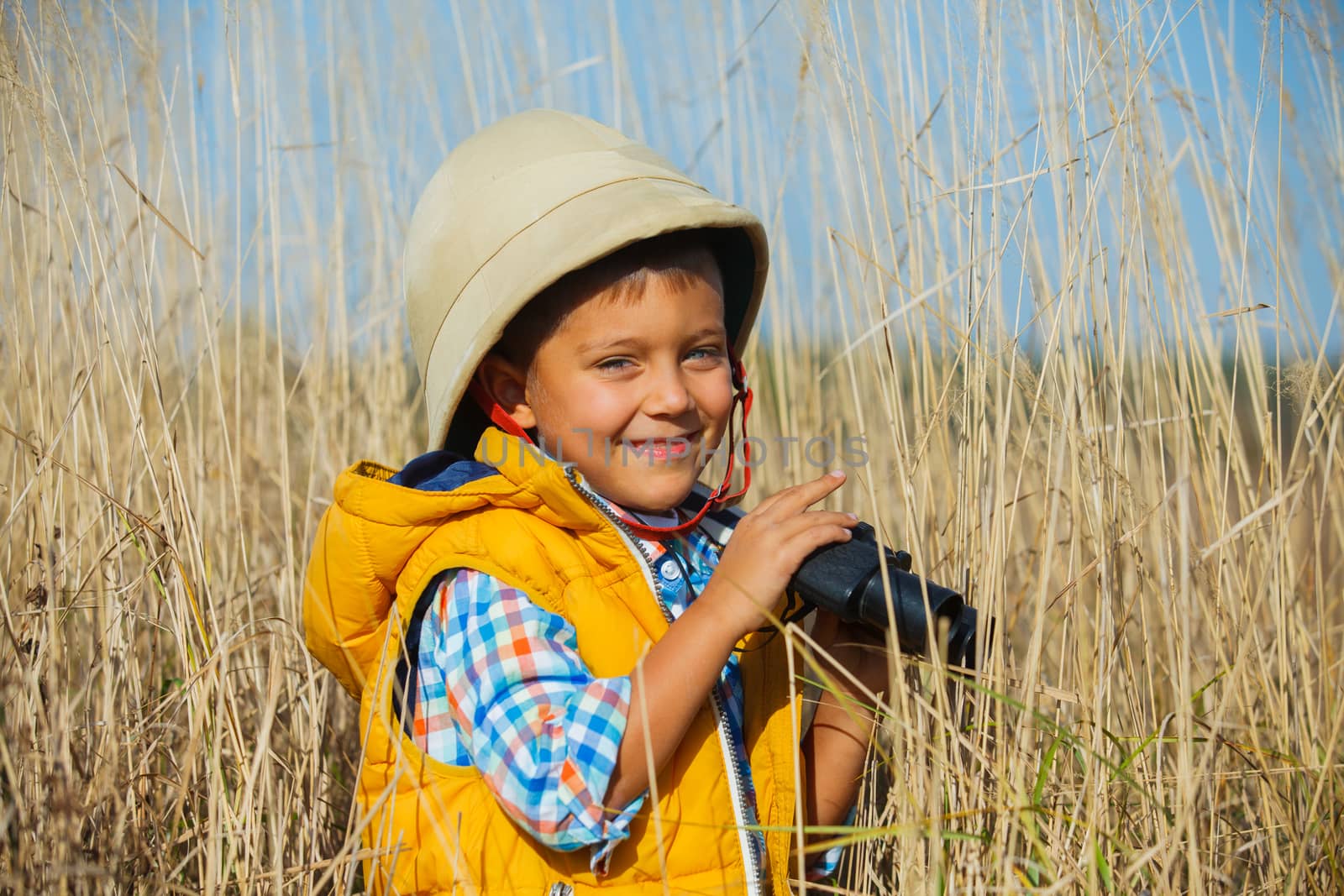 Young boy child playing pretend explorer adventure safari game outdoors with binoculars and bush hat