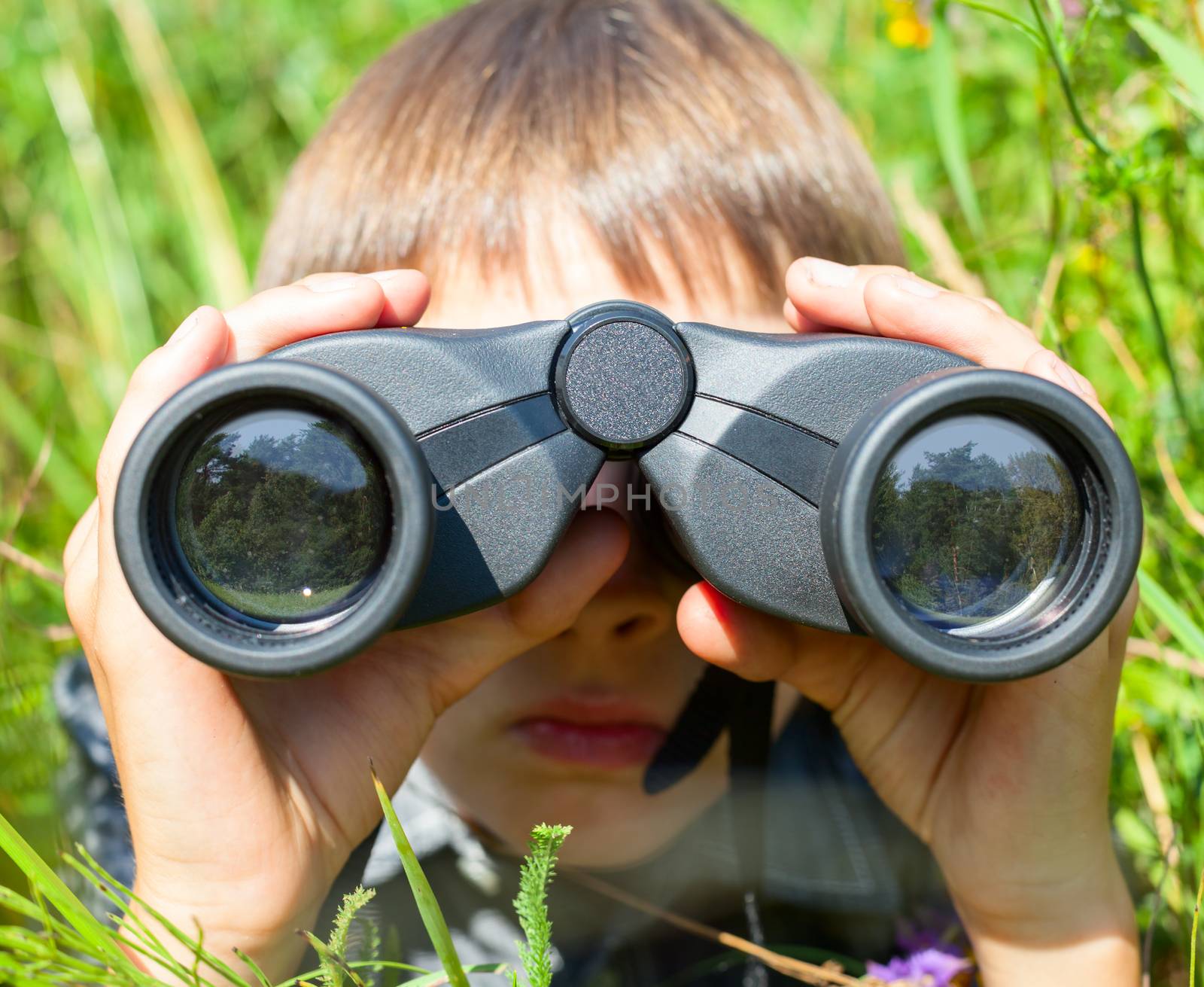Boy hiding in grass looking through binoculars outdoor