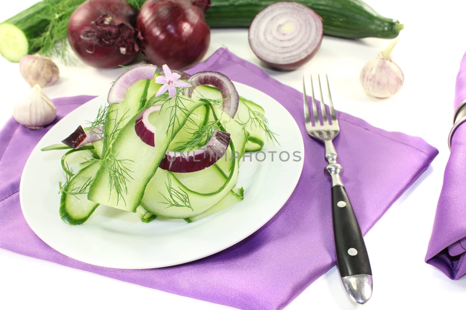Cucumber salad with red onions, garlic flower and dill on light background
