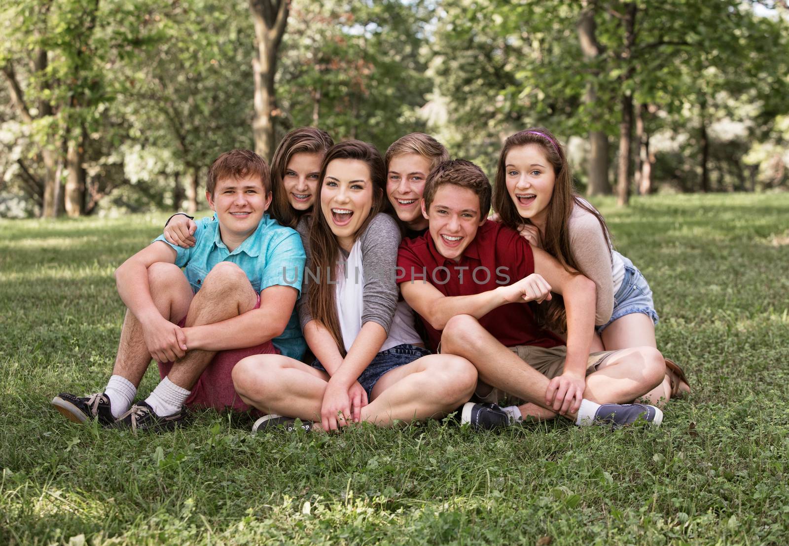 Happy group of European teenagers sitting on grass