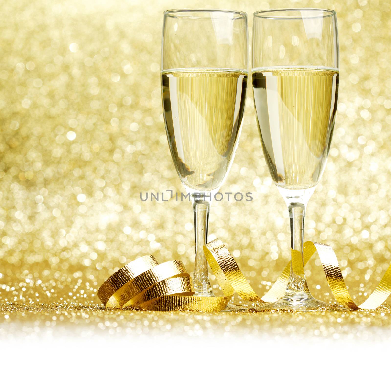 Glasses of champagne and curly decorative ribbon on golden glitters