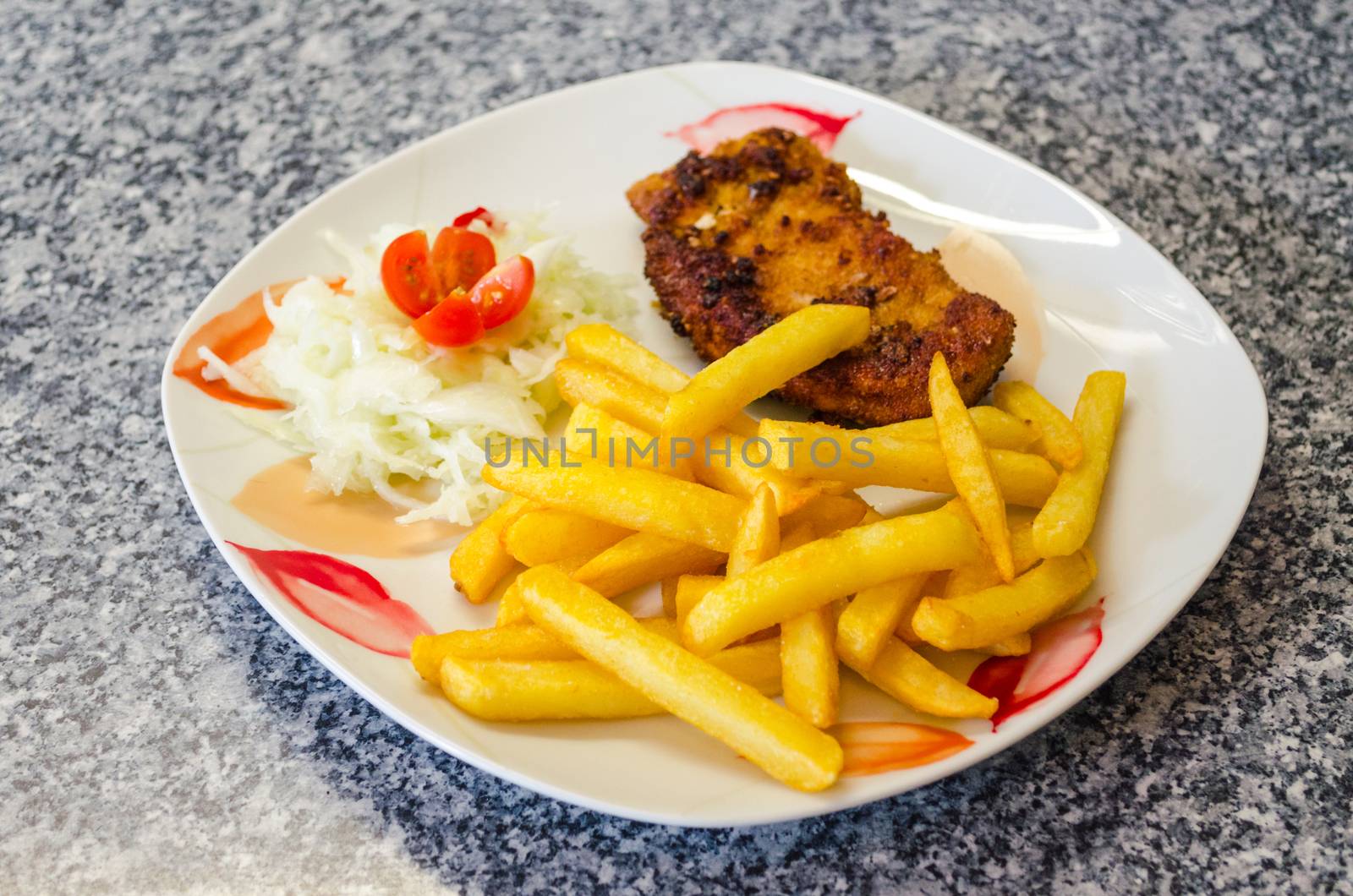 White plate with floral pattern on a schnitzel with chips and salad
