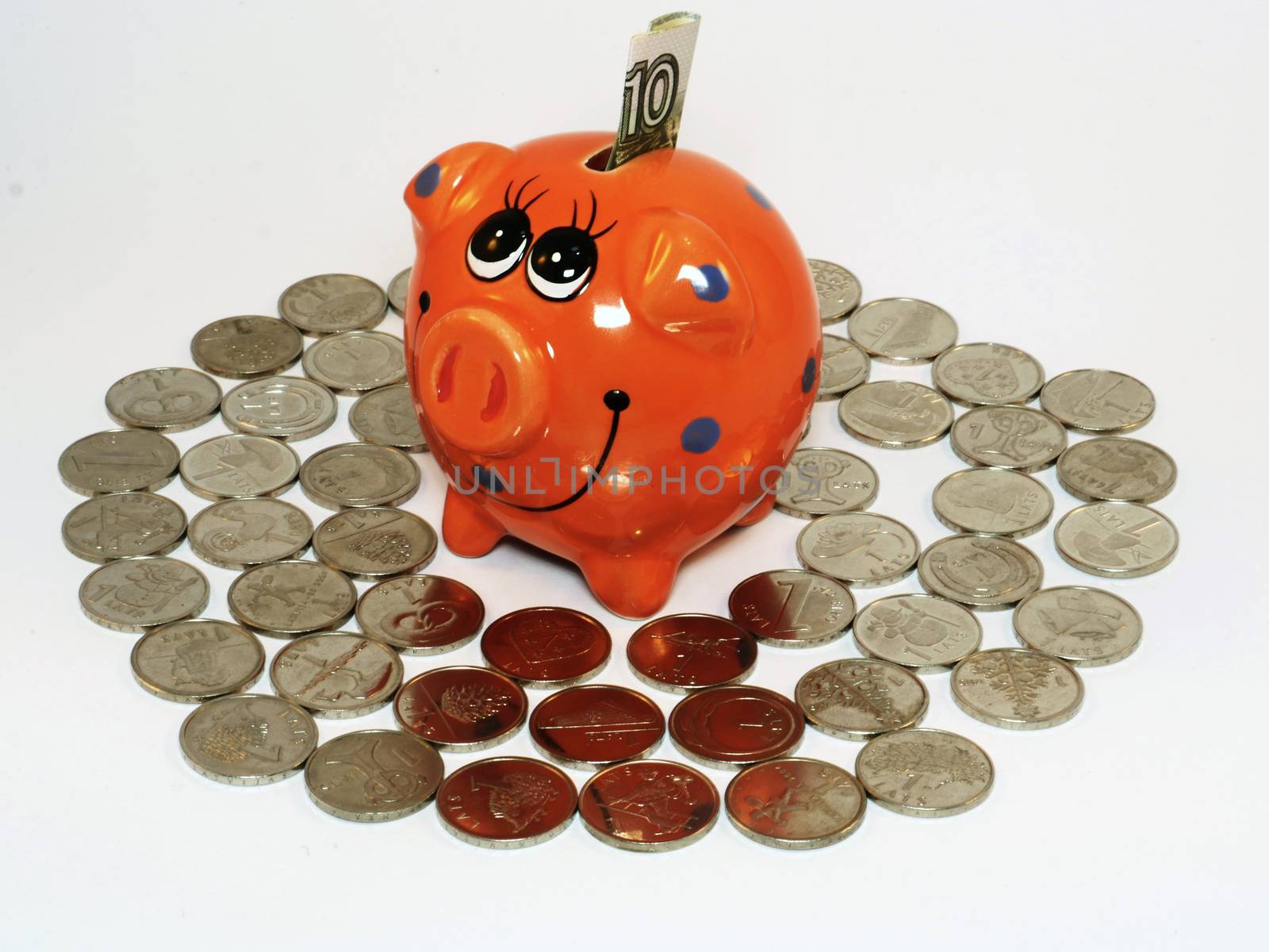 Bunch of Latvian lat coins and piggy bank on white background