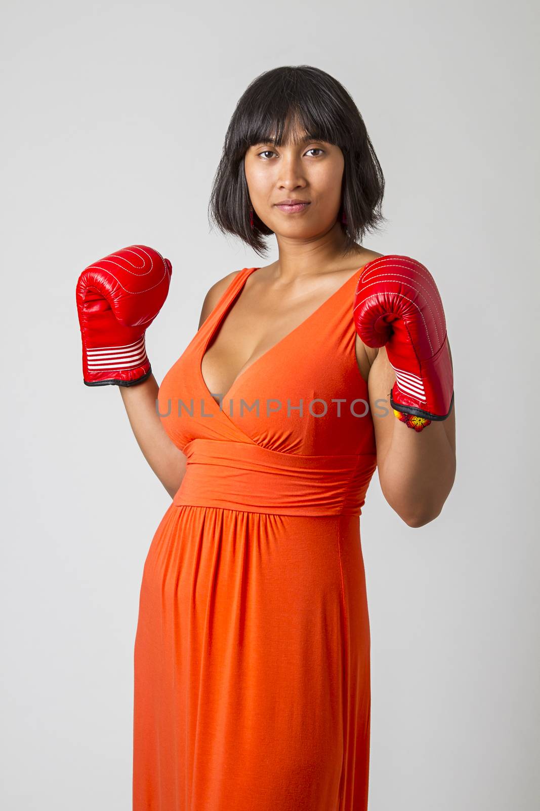 Young asian woman wearing a low cut orange dress, with her fist up wearing red boxing glove