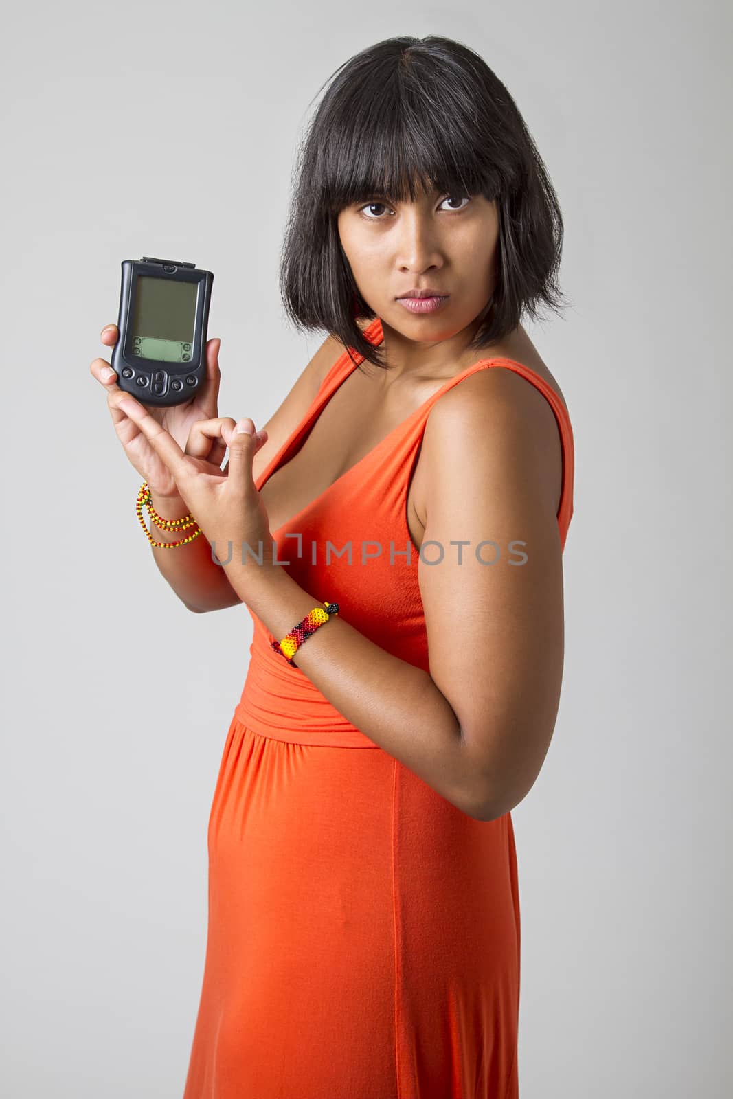 Young asian woman wearing a low cut orange dress, holding up an old personal digital assistant