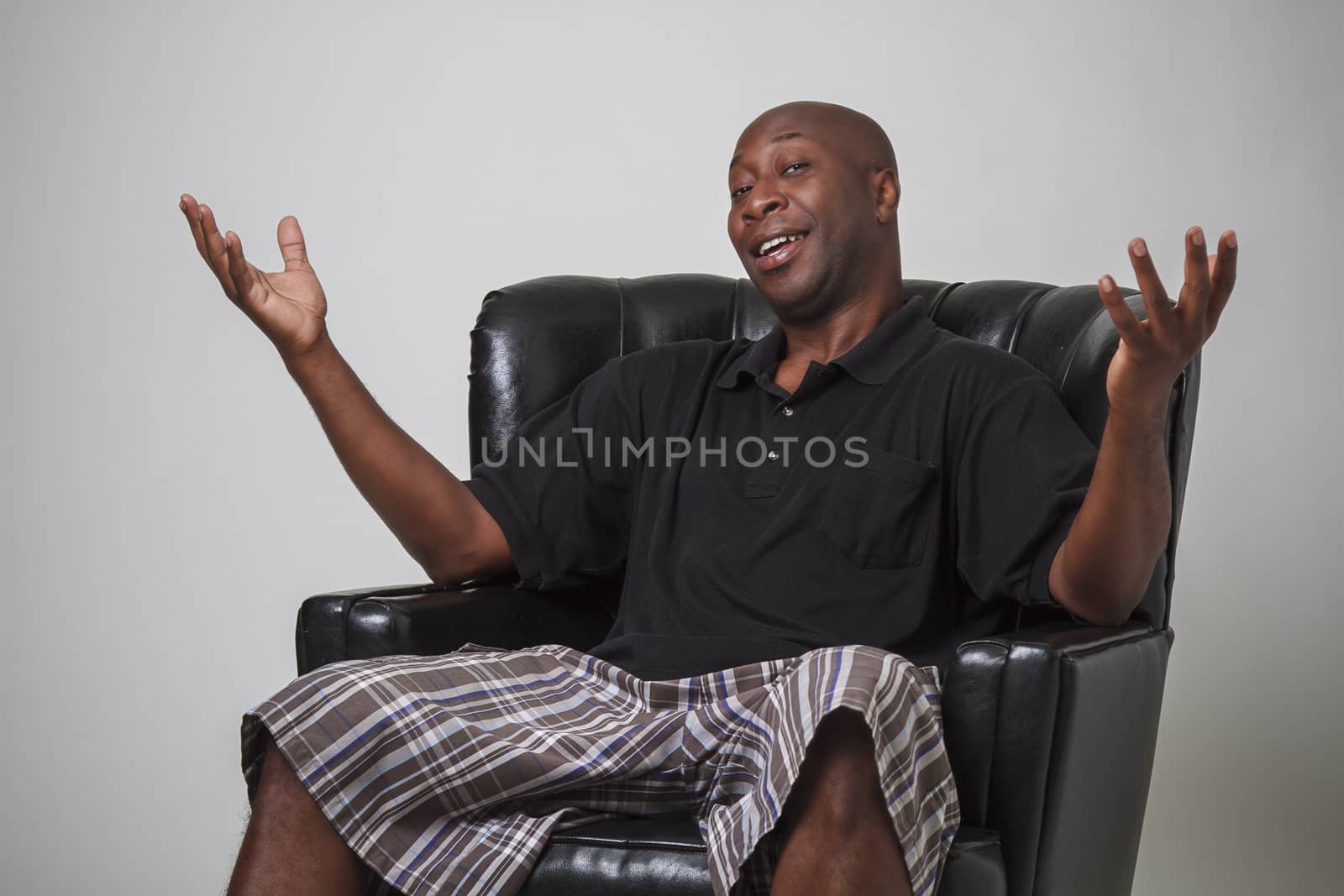 Forty year old black man, sitting on a leather chair, with his arm in the air and a smile