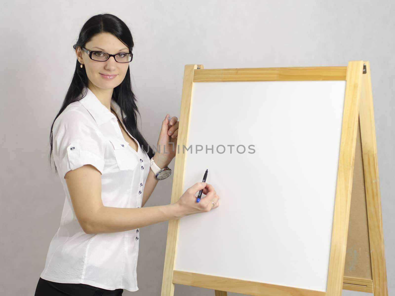 Working Girl in glasses writes a marker on a white board, looking at the camera. Studio, white background