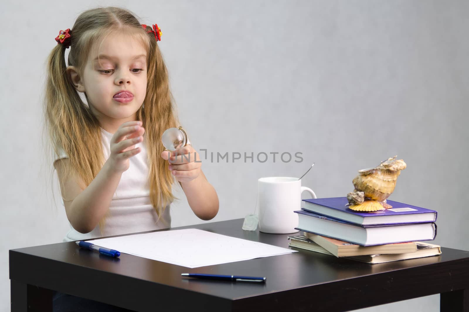 girl thoughtfully and effortlessly turns a small glass globe, sitting at the table. There are tombs of books, sheets of paper, a pen, glass globe, with a glass of tea, sea shell. The image of the writer.